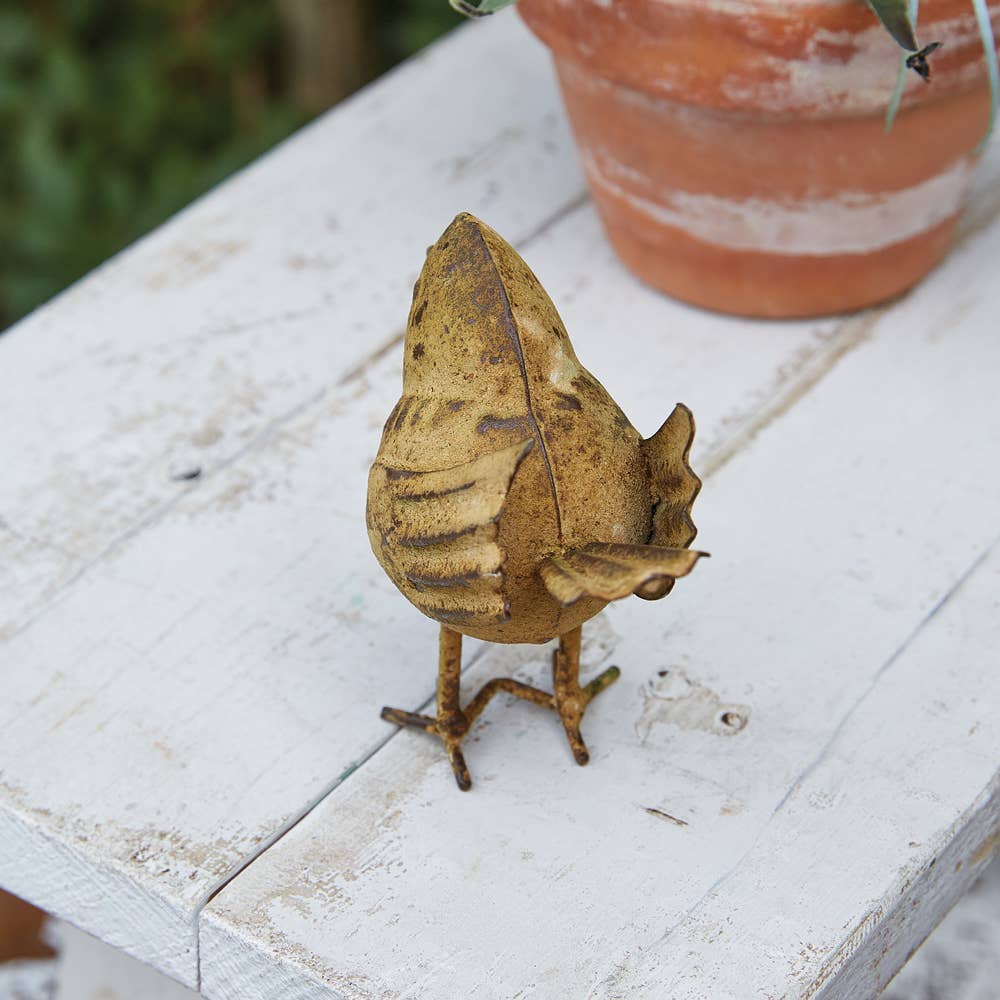 Brown leaf-shaped sculpture on a white wooden surface with a blurred plant pot in the background