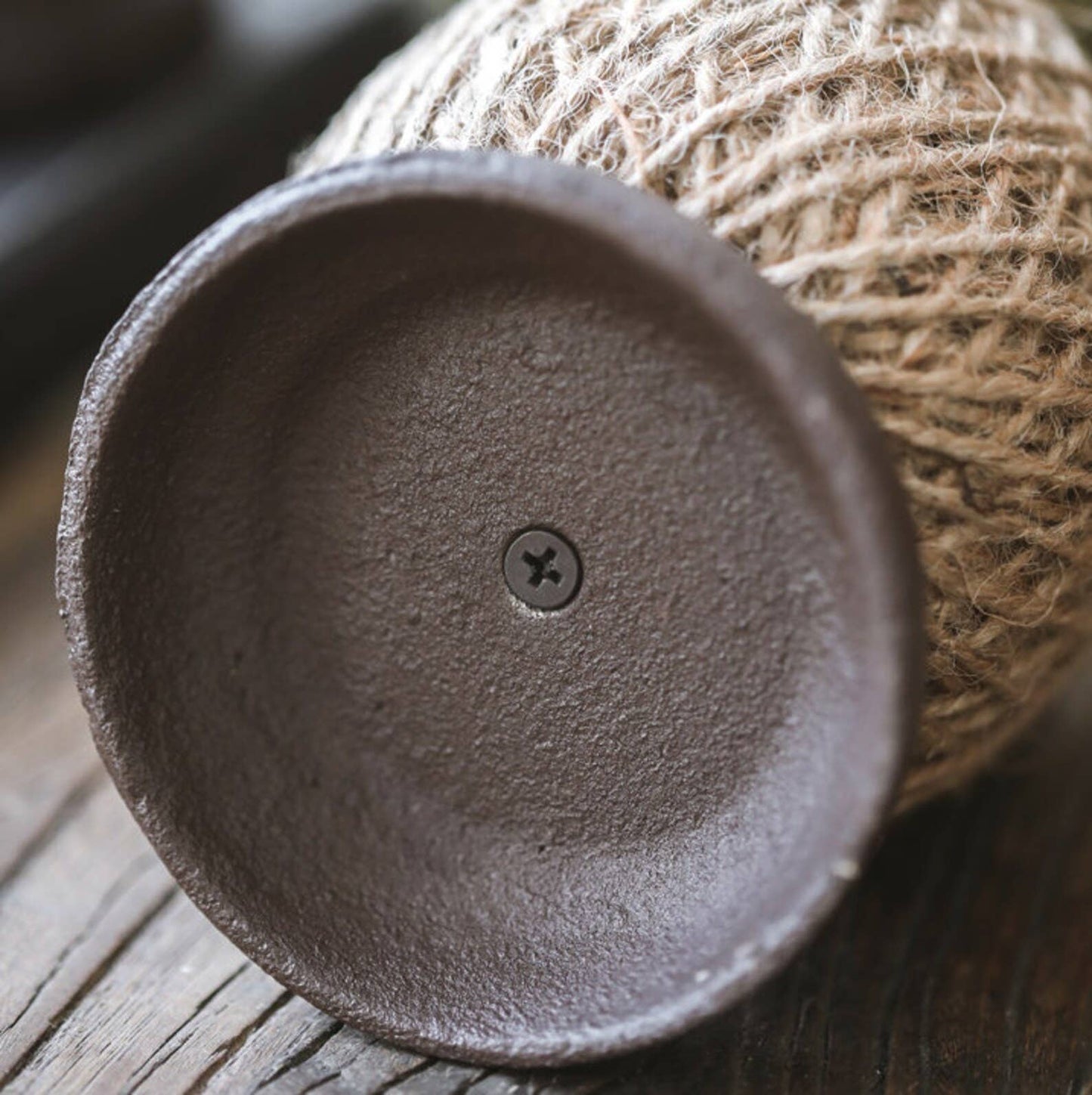 Close-up of a textured ceramic bowl with a small screw on a wooden surface