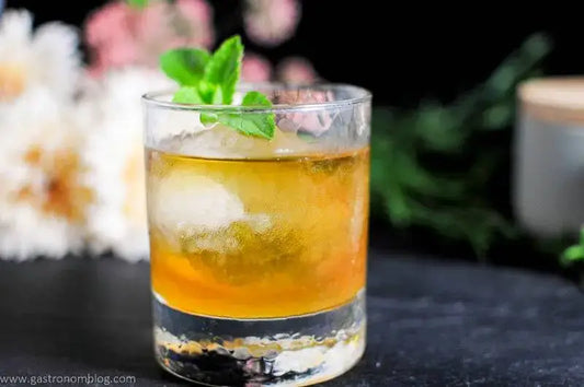 Cocktail with ice and mint garnish in a glass on a dark surface.