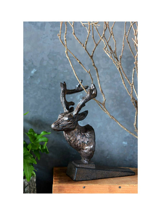 Decorative deer sculpture on a wooden surface with a blue wall and branches in the background