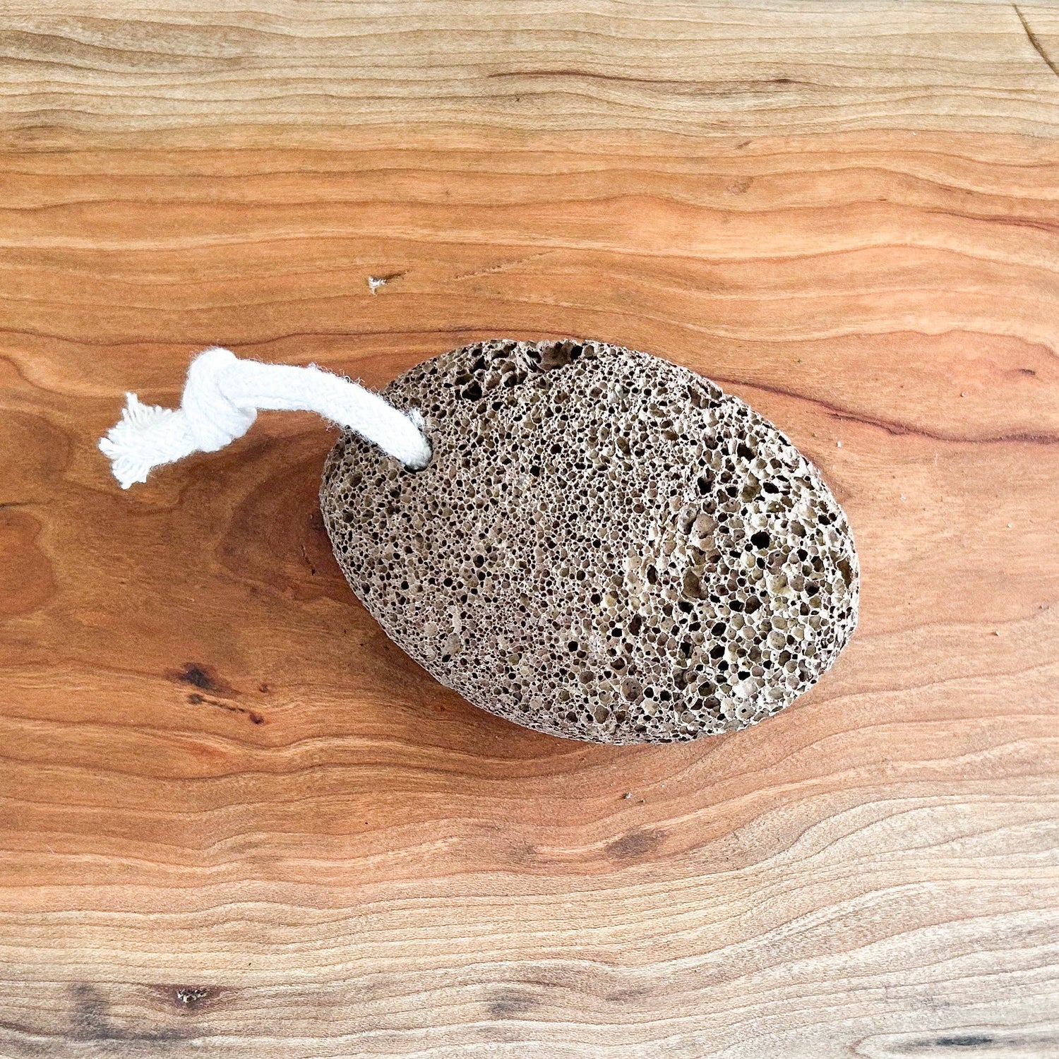 Pumice stone on a wooden surface with a small amount of white cream-like substance next to it.