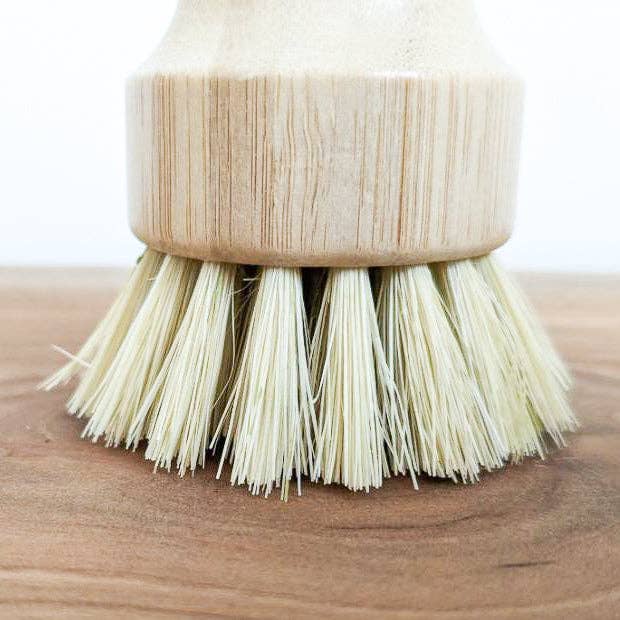 Dish brush with wooden handle and natural bristles on a wooden surface