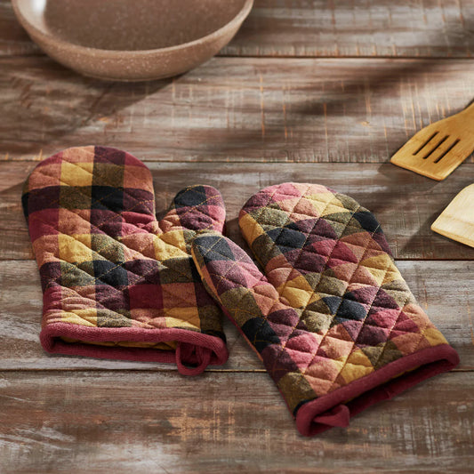 Pair of quilted oven mitts with autumnal pattern on a wooden surface.