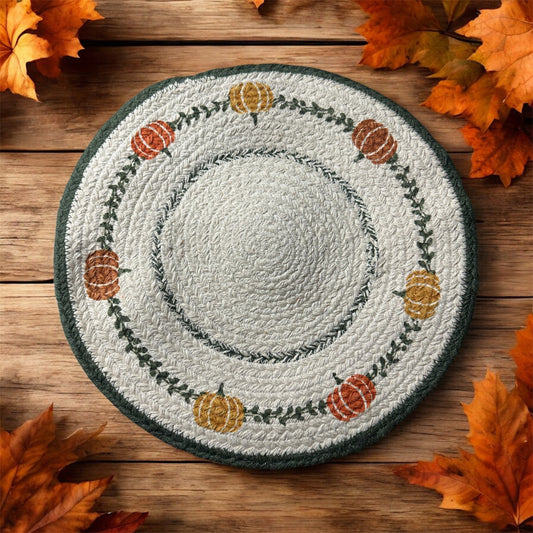 Round woven trivet with pumpkin design on a wooden surface with autumn leaves.