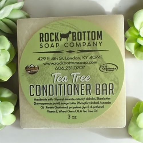 Rock Bottom Soap Company Tea Tree Conditioner Bar on a white background with green leaves.