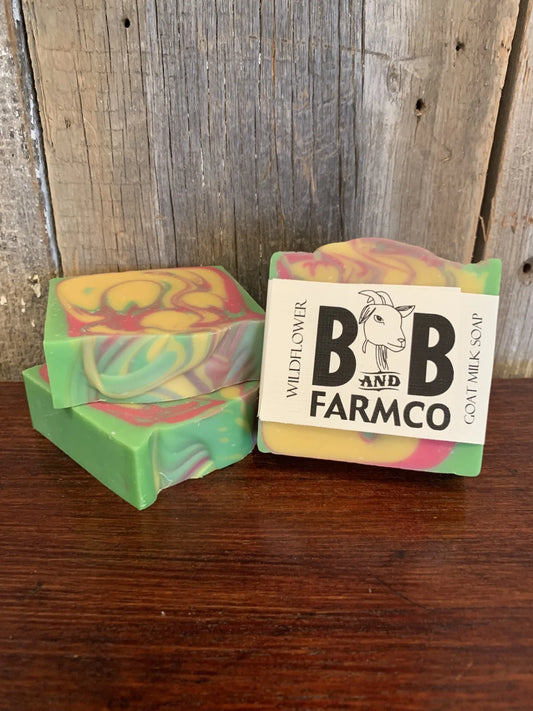 Colorful soap bars with a 'B & B Farmco' label on a wooden surface and background.