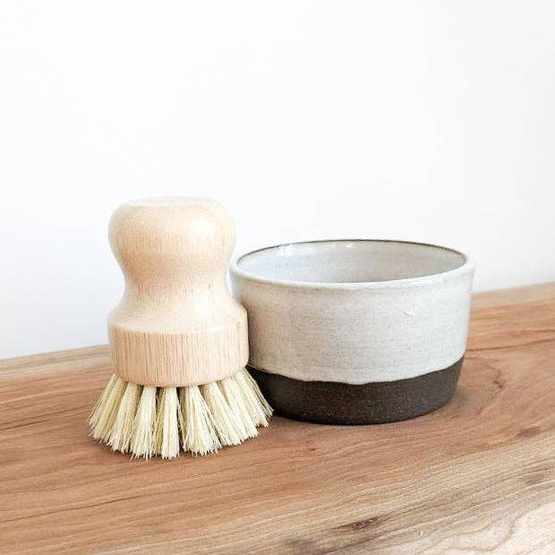 Dish brush and ceramic bowl on a wooden surface with a white background