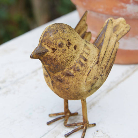Rust-colored metal bird figurine on a white surface with a blurred background
