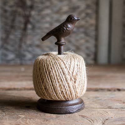 Decorative item with a ball of twine and a metal bird on top, placed on a wooden surface.